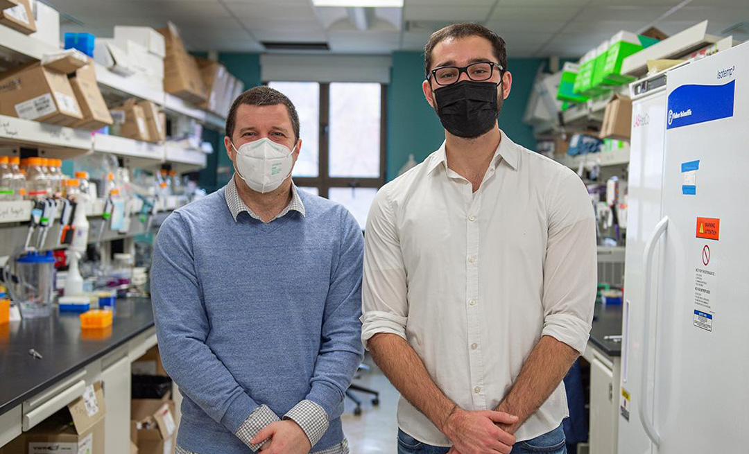Justin Pritchard and Scott Leighow wearing masks sanding with hands in front of them in a lab